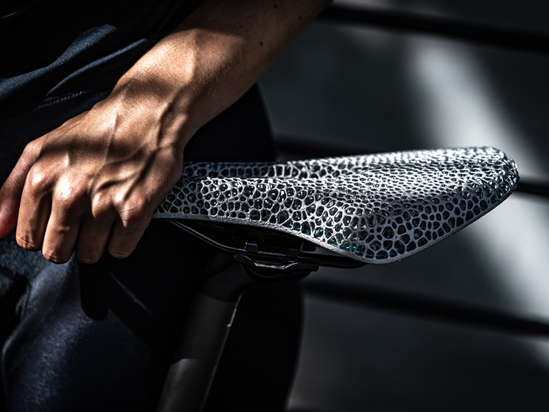 Close-up of a white woman's hand holding part of the grey 3D printed bicycle saddle with a custom lattice structure.